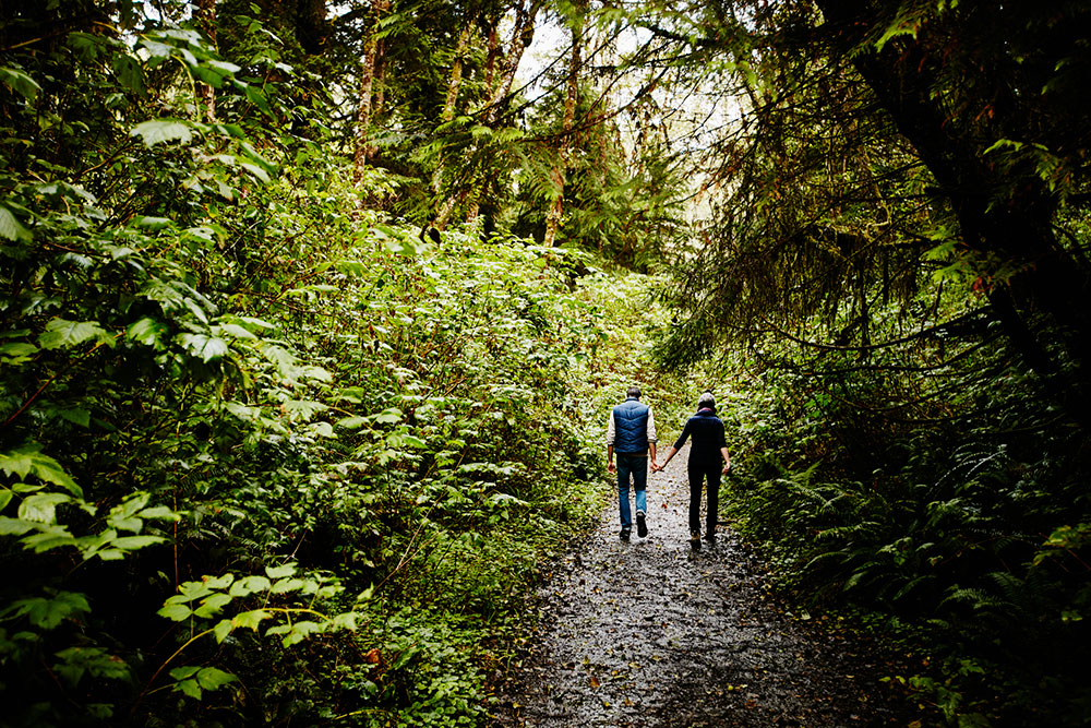 A couple holding hands while walking along a trail in the forest.