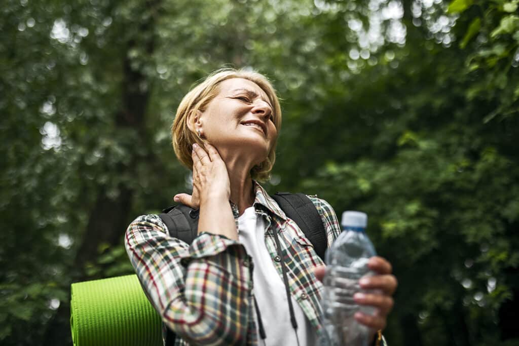 A female hiker in the woods, rubbing her neck due to a mosquito bite.