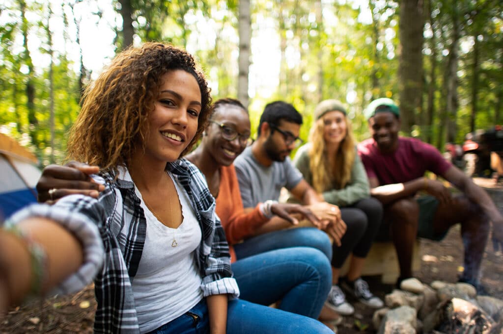 A group of hikers sitting on a long log besides a bonfire pit. 